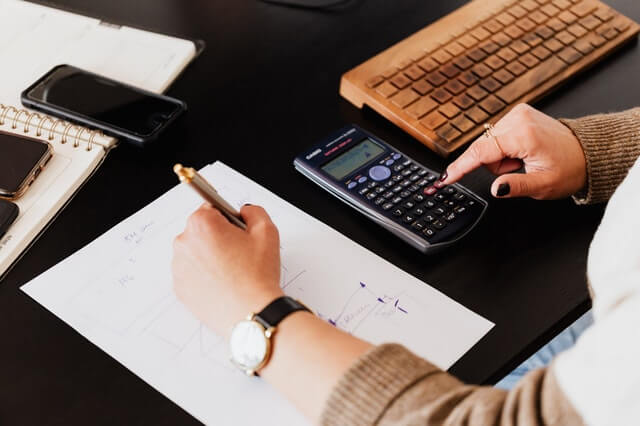 Crop woman using calculator and taking notes on paper